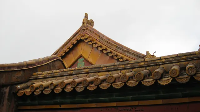 A curved tiled ridge rises behind a lower line of round tile ends, with small roof ornaments against a pale sky.