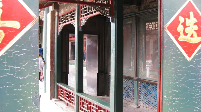 Dark red carved latticework frames an entrance between weathered green panels decorated with red diamond-shaped signs.