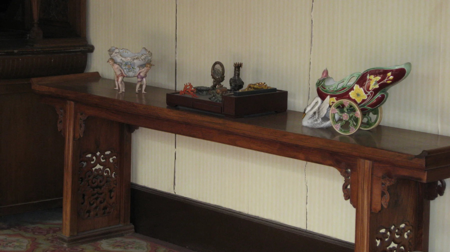 Small decorative objects sit along a narrow wooden table with carved supports against a pale interior wall.