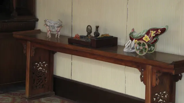 Small decorative objects sit along a narrow wooden table with carved supports against a pale interior wall.