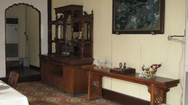 A carved wooden cabinet and a long side table stand beneath a framed picture in a room with a patterned floor.