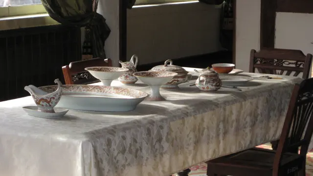 A closer view of a dining table shows decorated dishes, bowls and serving pieces arranged on a pale cloth.