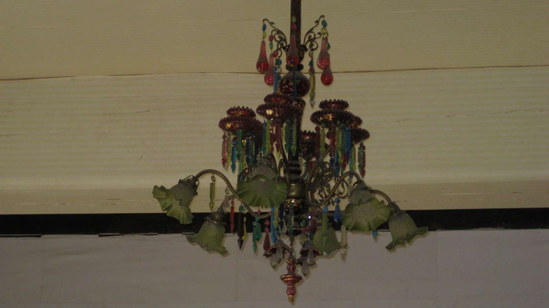 An ornate hanging light has greenish shades, coloured decorations and dangling ornaments beneath a pale ceiling.