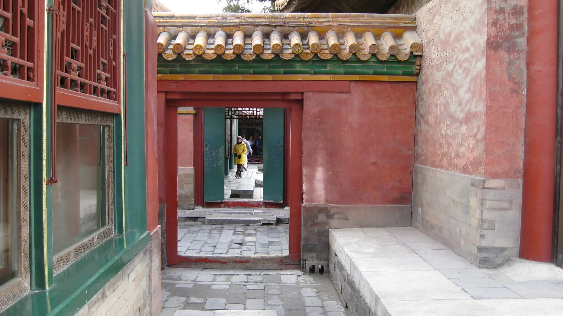 A paved passage between red walls leads through a sequence of open rectangular doorways, with lattice windows on the left.