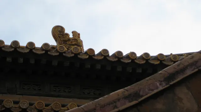 A curled decorative figure rises above a row of rounded roof tiles, with overlapping eaves against a pale sky.