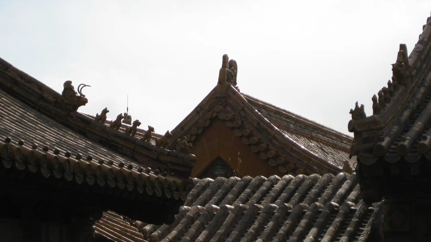 Small roof figures and curled ridge ornaments rise above intersecting rows of dark and golden tiles.