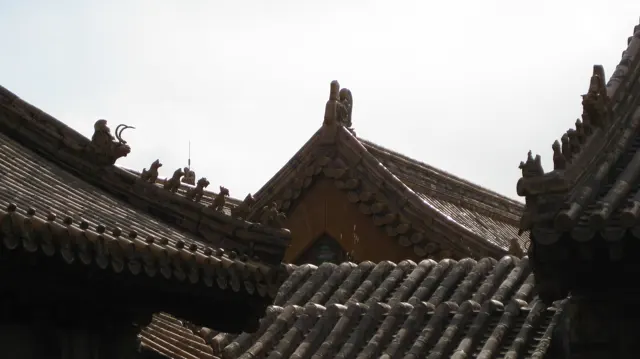Small roof figures and curled ridge ornaments rise above intersecting rows of dark and golden tiles.