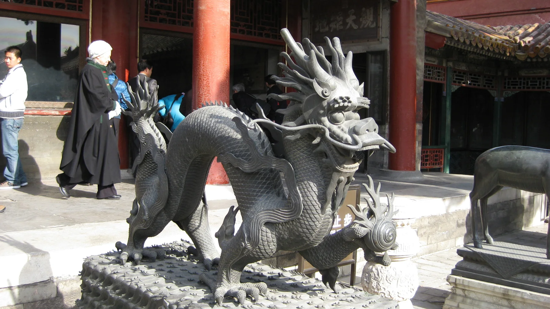 A dark sculpted dragon with an open mouth and raised horns stands on a decorated base in front of red columns.