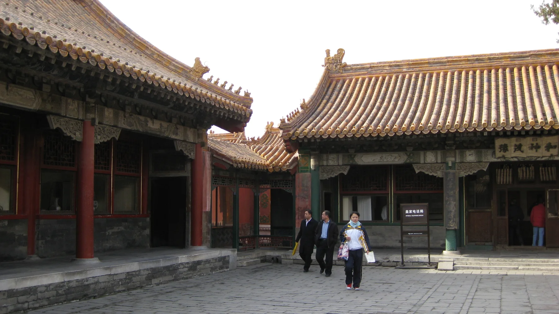 Visitors cross a stone-paved courtyard between red-columned buildings with curved tiled roofs.
