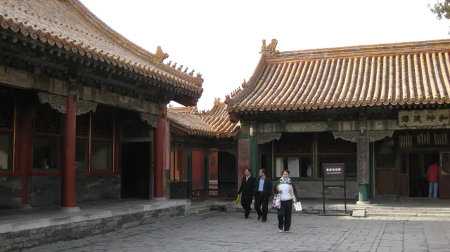 Visitors cross a stone-paved courtyard between red-columned buildings with curved tiled roofs.