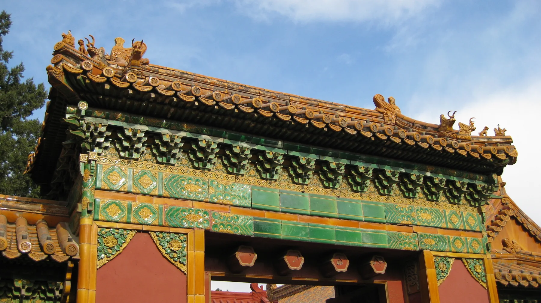 An ornate gateway is decorated with green, gold and turquoise panels beneath a curved golden-tiled roof.