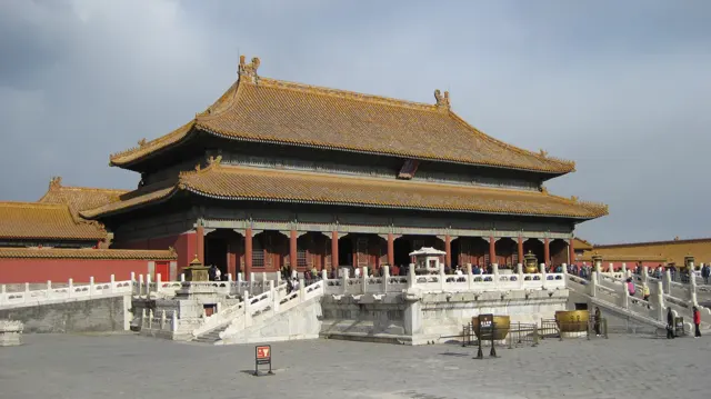 A large red-columned hall with a double-tiered golden roof stands above a white stone terrace and stairways.