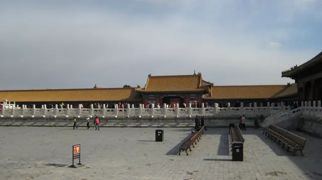 A broad stone-paved courtyard extends towards a distant gateway, bordered by white balustrades and golden-roofed buildings.