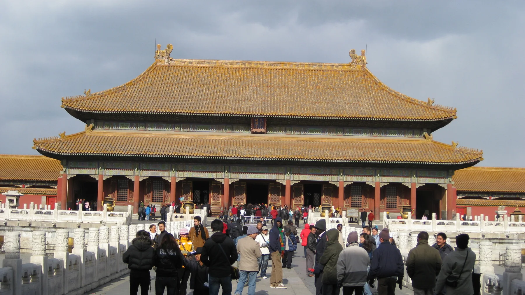 Visitors move towards a large golden-roofed hall along a route bordered by white stone balustrades.