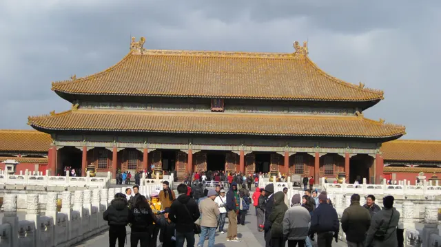 Visitors move towards a large golden-roofed hall along a route bordered by white stone balustrades.