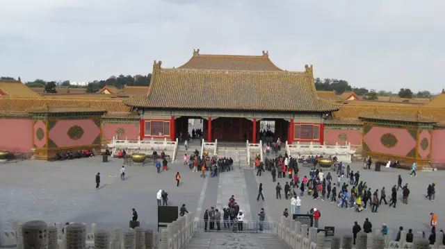 An elevated view looks across a courtyard towards a broad golden-roofed gateway, with visitors spread along the paved approach.