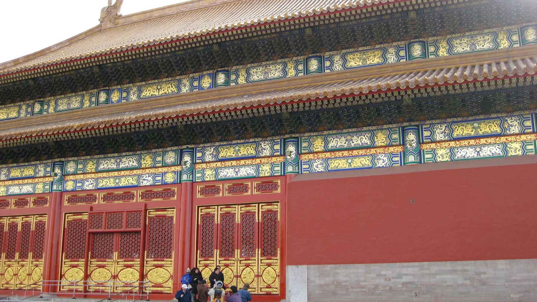 Bands of blue, green and gold decoration run above tall red doors and lattice panels, with visitors gathered below.
