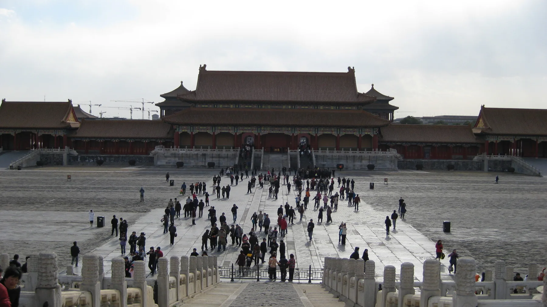 A stream of visitors crosses a broad courtyard towards a large red gateway, seen from above a stone stairway.