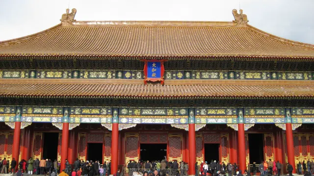 Golden roof tiles and richly painted horizontal beams rise above red columns and busy open entrances.
