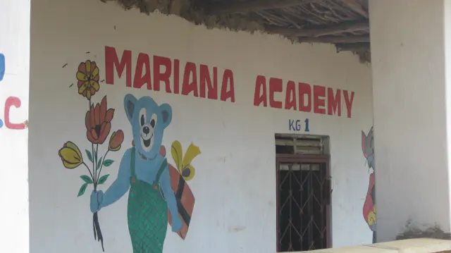 Red school lettering and a painted blue character holding flowers decorate a white wall beside a doorway marked KG 1.