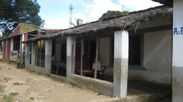 A row of low buildings with shaded doorways and white veranda pillars runs beside an unpaved courtyard.