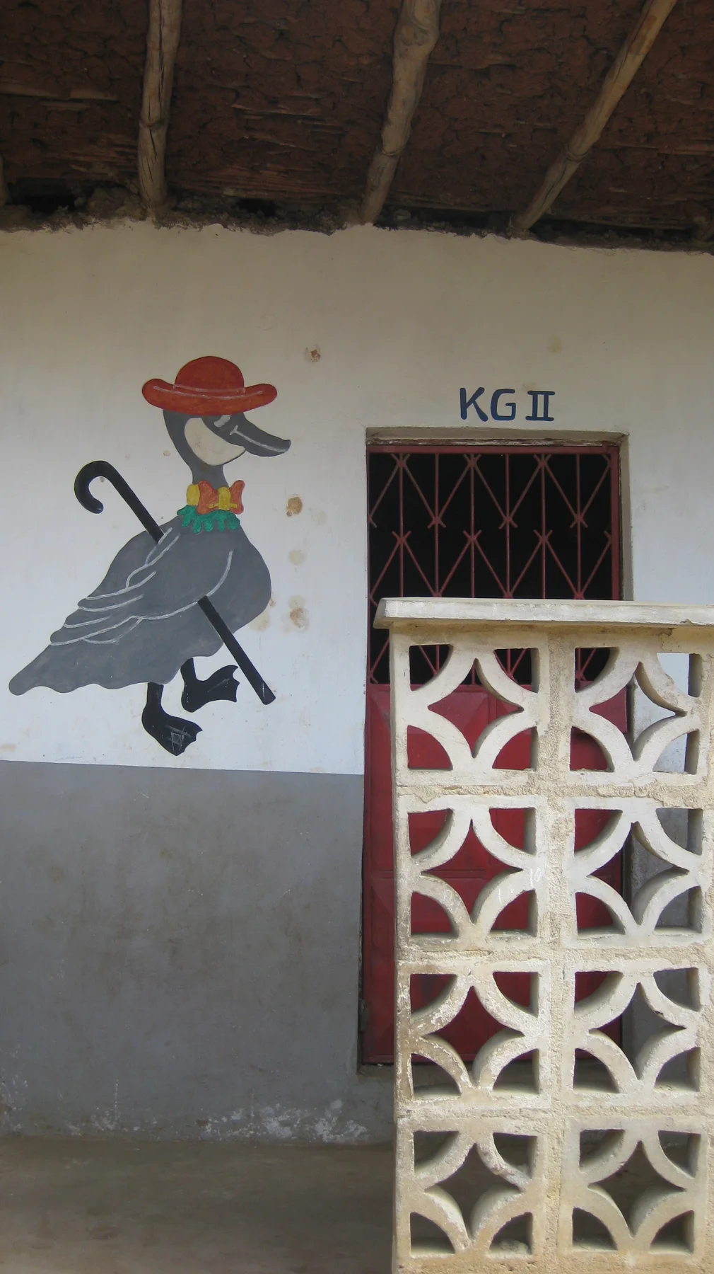 A painted cartoon figure appears on a white wall beside a doorway marked KG 1 and a section of patterned concrete screening.
