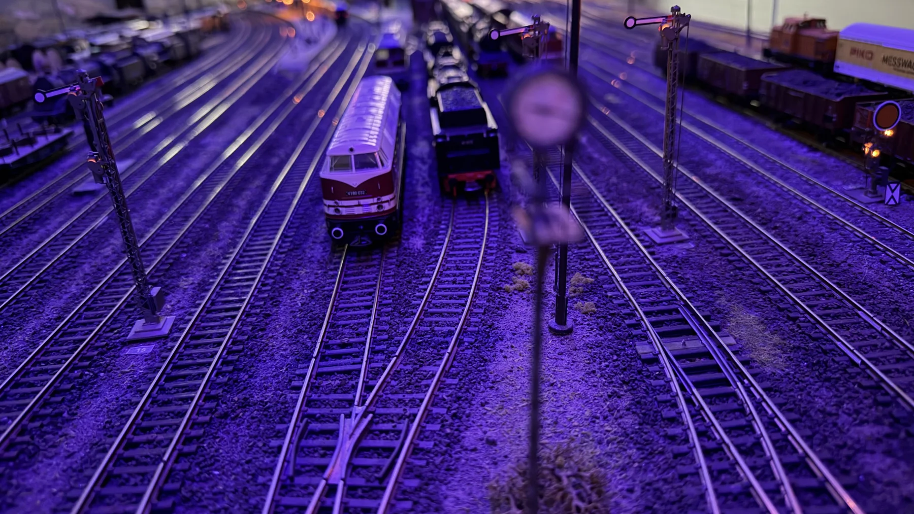 Parallel tracks and model locomotives are lit by violet exhibition lighting.