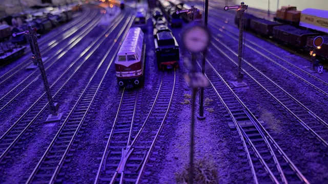 Parallel tracks and model locomotives are lit by violet exhibition lighting.