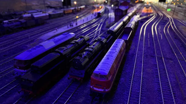 Rows of model trains and curving tracks glow under blue and violet lighting.