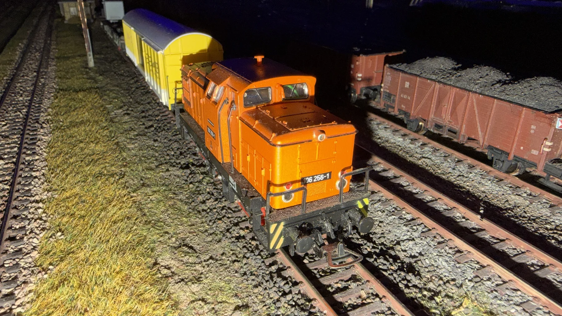 An orange model shunting locomotive stands in front of yellow and white freight wagons.