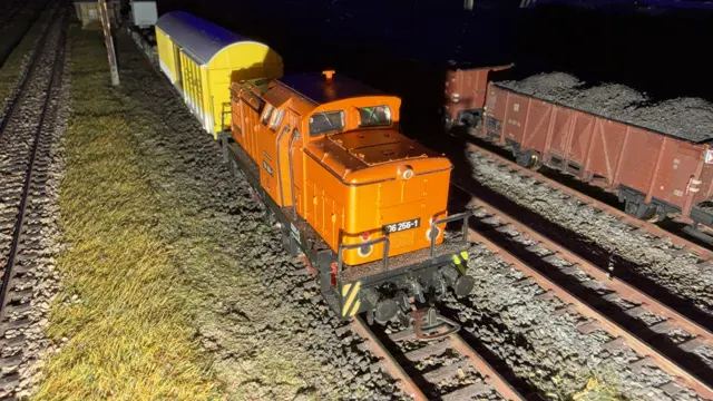 An orange model shunting locomotive stands in front of yellow and white freight wagons.