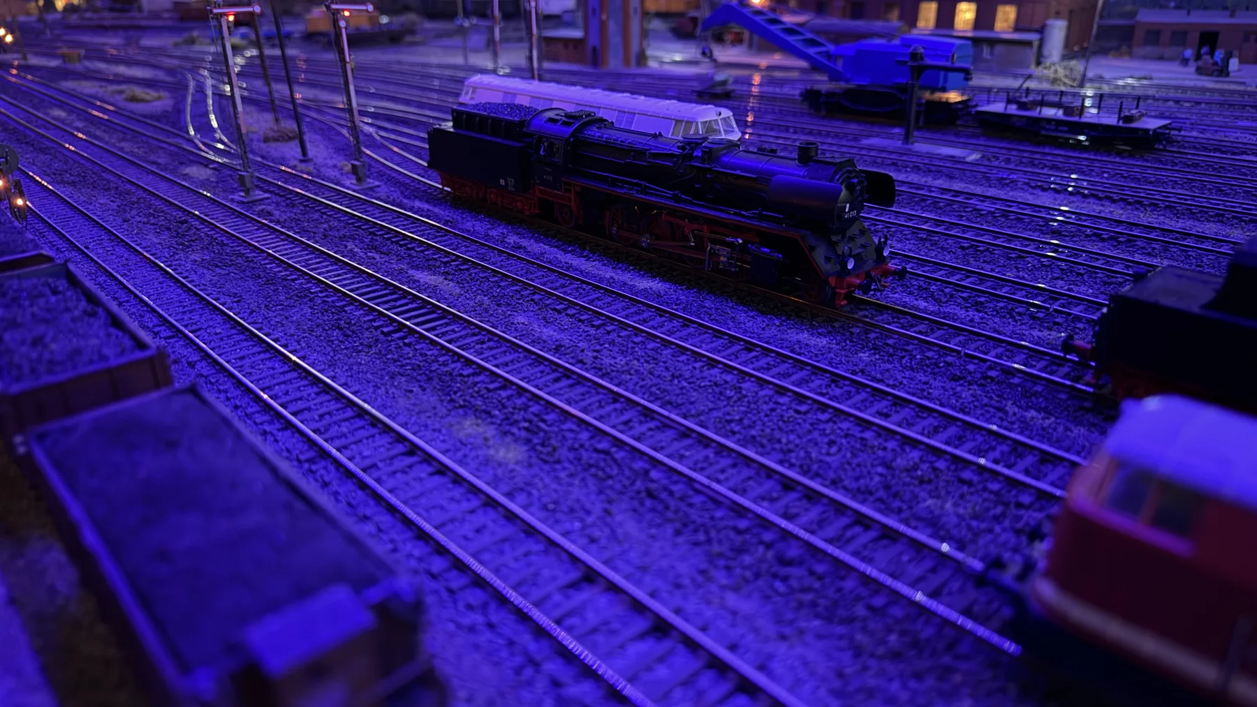 A dark model steam locomotive and tender sit on tracks under blue exhibition lighting.