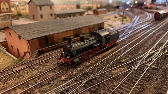 A black model steam locomotive stands beside a long brick-coloured railway shed.