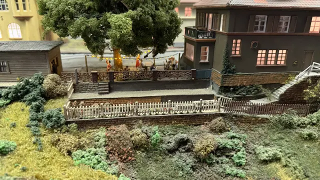 Small fenced gardens and miniature figures sit beside model houses and trees.