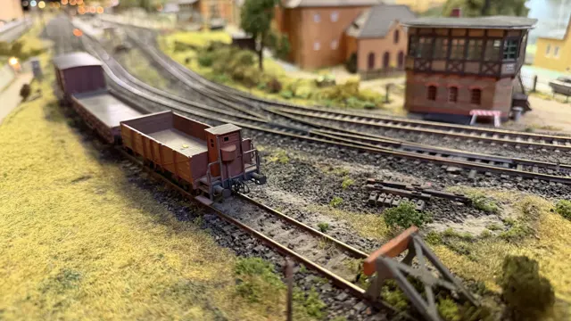 A brown model freight wagon stands near a buffer stop beside curving tracks.