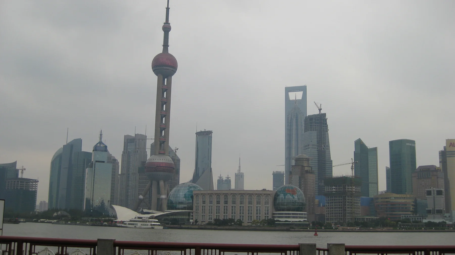 A skyline of tall buildings and a tower with spherical sections rises across a broad river beneath a grey sky.