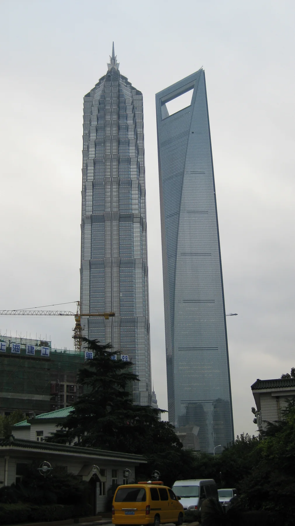 A pair of skyscrapers rises above a street with vehicles, one topped by a narrow spire and the other by a rectangular opening.