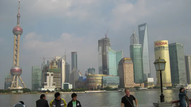 Visitors stand along the riverfront beneath a skyline of glass towers, with a tall spherical-section tower at the left.