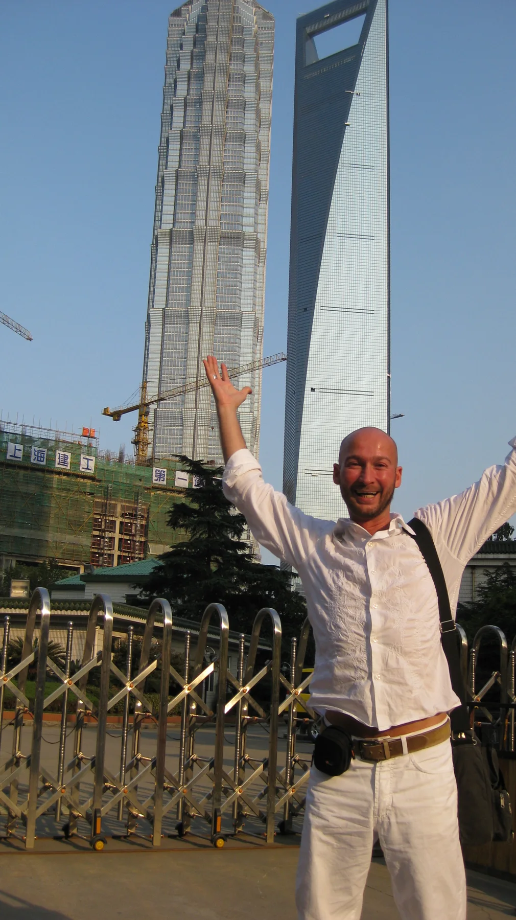 A person raises both arms beneath two skyscrapers, framed by a blue sky in a portrait composition.