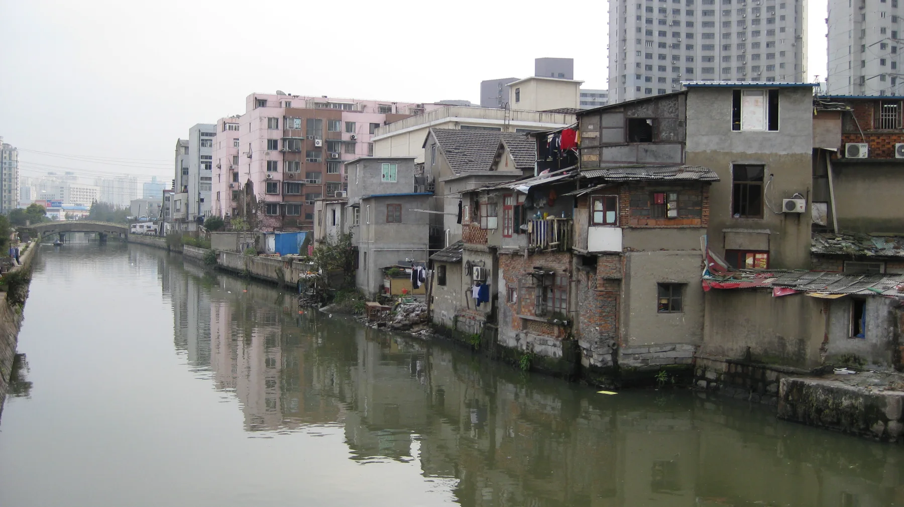 Closely packed buildings line a narrow canal, their walls reflected in still greenish water.