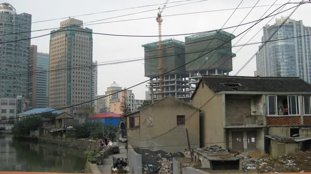 Low tiled roofs and tangled overhead cables cross the foreground, with high-rise buildings and construction behind.