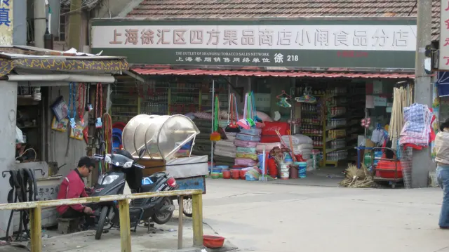 Buckets, brushes and household goods fill a shopfront beside scooters and a railing.