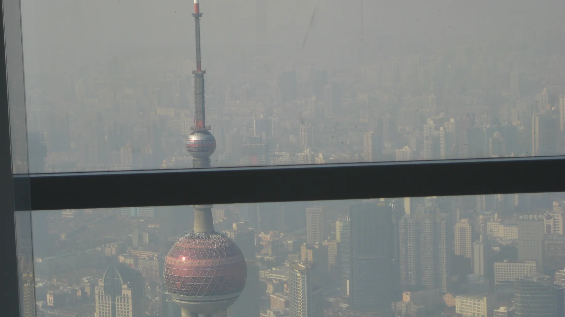 A tower with spherical sections is seen through an observation window divided by a dark horizontal frame.