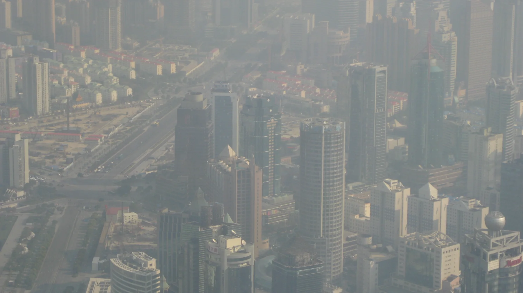 An elevated view looks down over dense buildings and a broad road through a veil of haze.