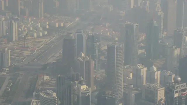 An elevated view looks down over dense buildings and a broad road through a veil of haze.