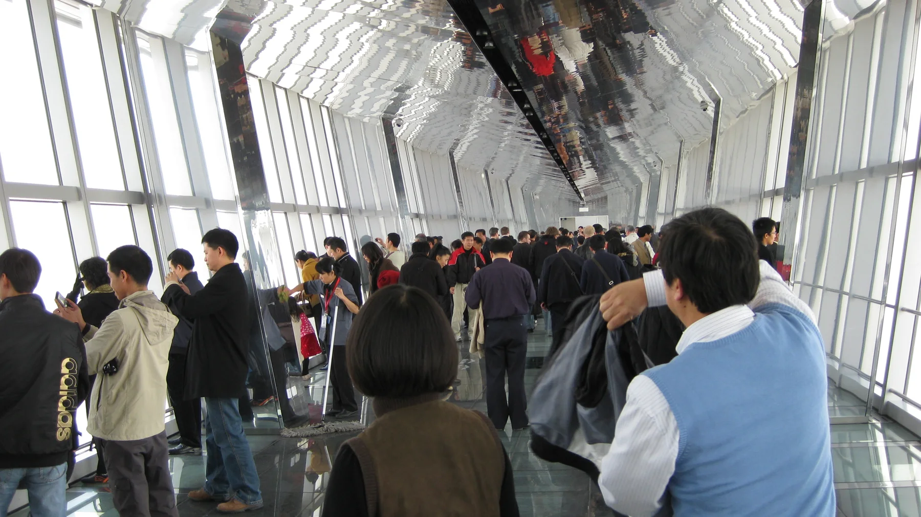 Visitors fill a long observation corridor with sloping windows, a reflective ceiling and a polished floor.