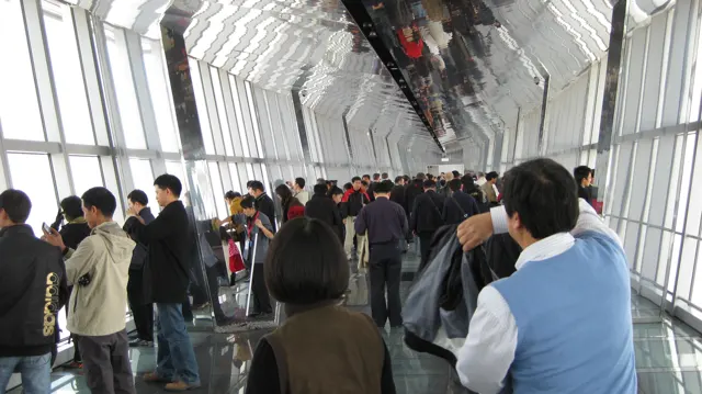 Visitors fill a long observation corridor with sloping windows, a reflective ceiling and a polished floor.