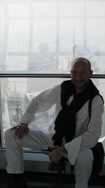 A person sits beside a large window, silhouetted against a pale city view far below.