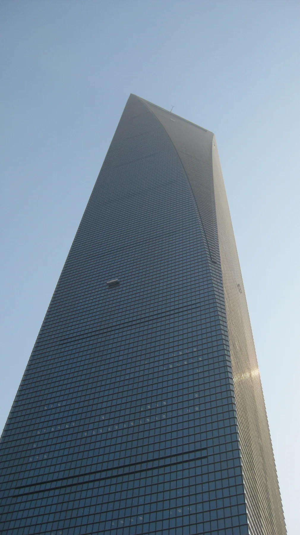 A glass skyscraper rises sharply against a blue sky, with sunlight catching one edge.