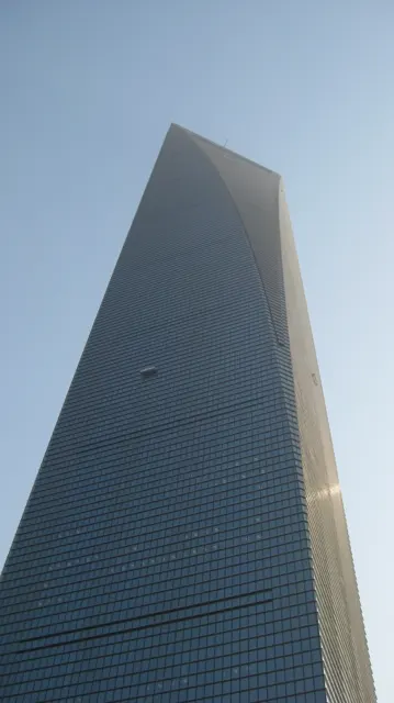 A glass skyscraper rises sharply against a blue sky, with sunlight catching one edge.